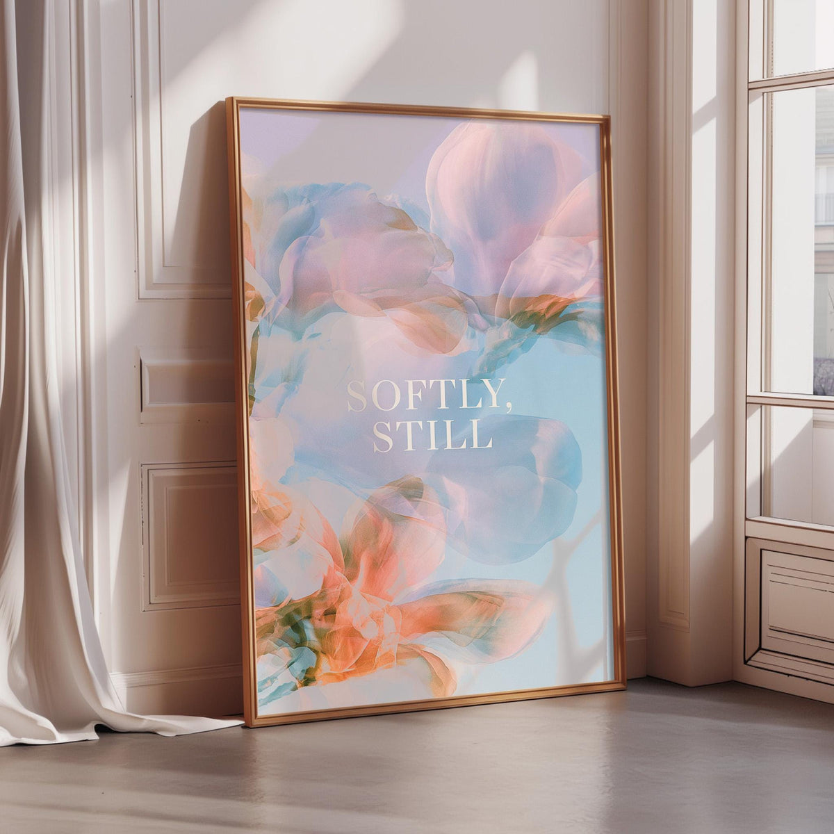 A framed poster with a floral design and the text "Softly, Still" is displayed in a room with a window.
