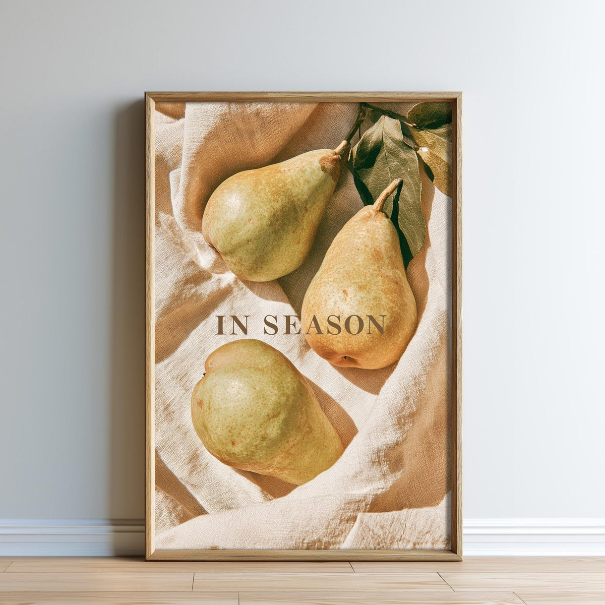 A framed image of three pears on a beige cloth, with the text "IN SEASON" displayed prominently in the center.