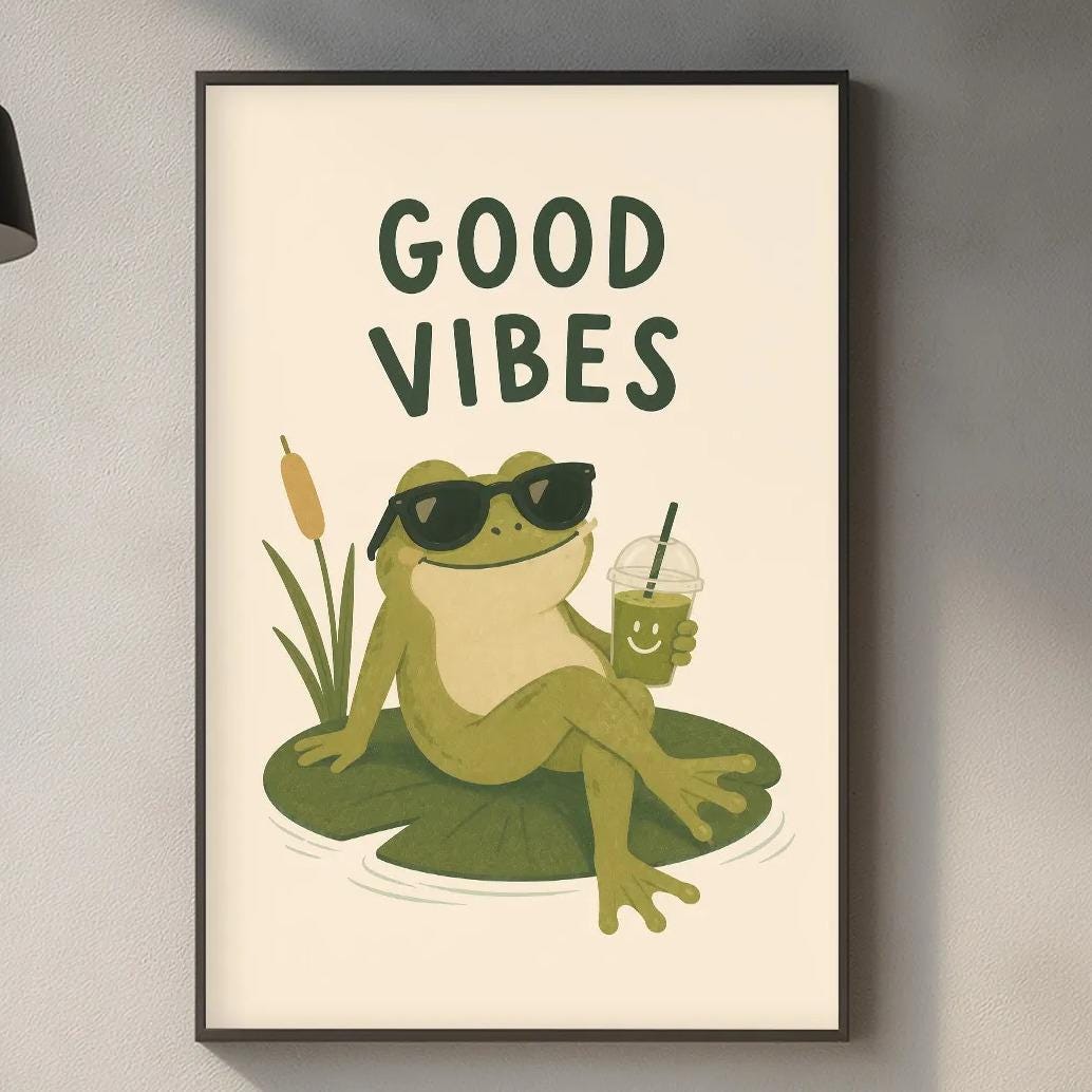 a framed poster of a frog sitting on a lily pad, wearing sunglasses and holding a drink, with the text "GOOD VIBES" above it. The poster is displayed on a wall above a kitchen counter with various kitchen items such as a cutting board, a bottle, and a plant.