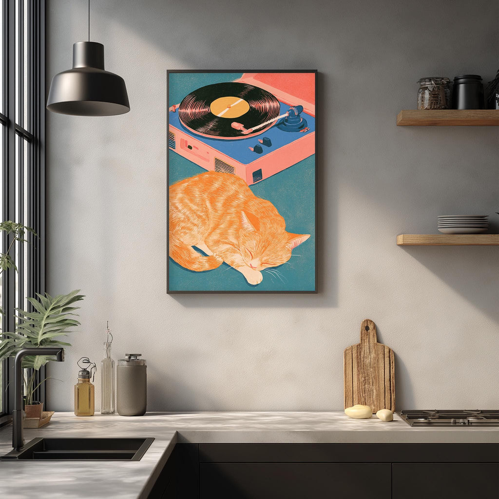 a kitchen counter with a framed painting of an orange cat sleeping on a record player, surrounded by various kitchen items such as a cutting board, a bottle, and a vase.