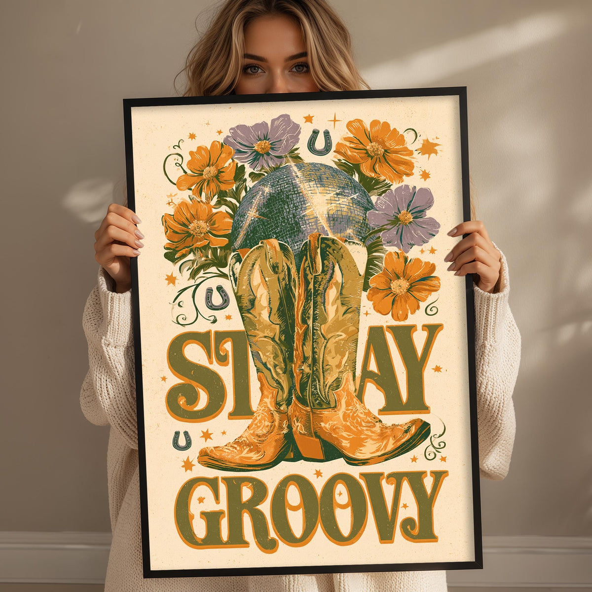 A woman holding a framed poster with a vibrant design featuring a pair of boots, flowers, and the text "STAY GROOVY".