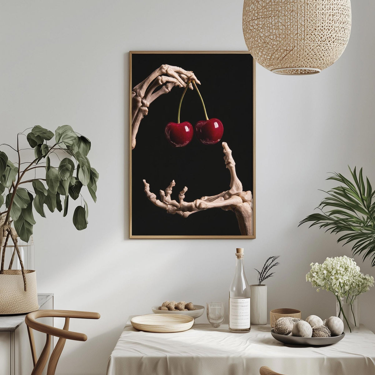 a minimalist dining room setting with a framed artwork of a skeleton hand holding cherries hanging on the wall above a table with various items on it.