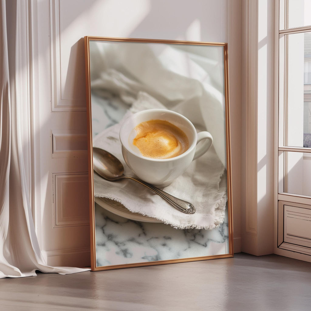 A framed photograph of a cup of coffee with foam on top, placed on a marble surface, with a spoon resting on a napkin.