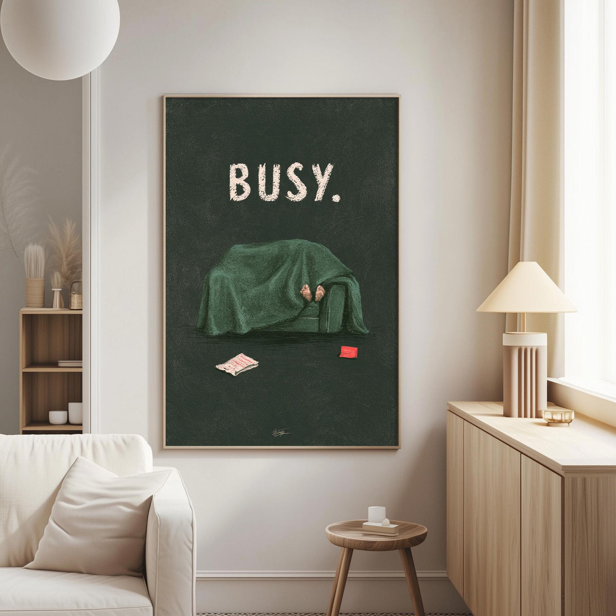 a cozy living room with a large framed poster of a person under a green blanket, sitting on a couch with a book and a red object on the floor.