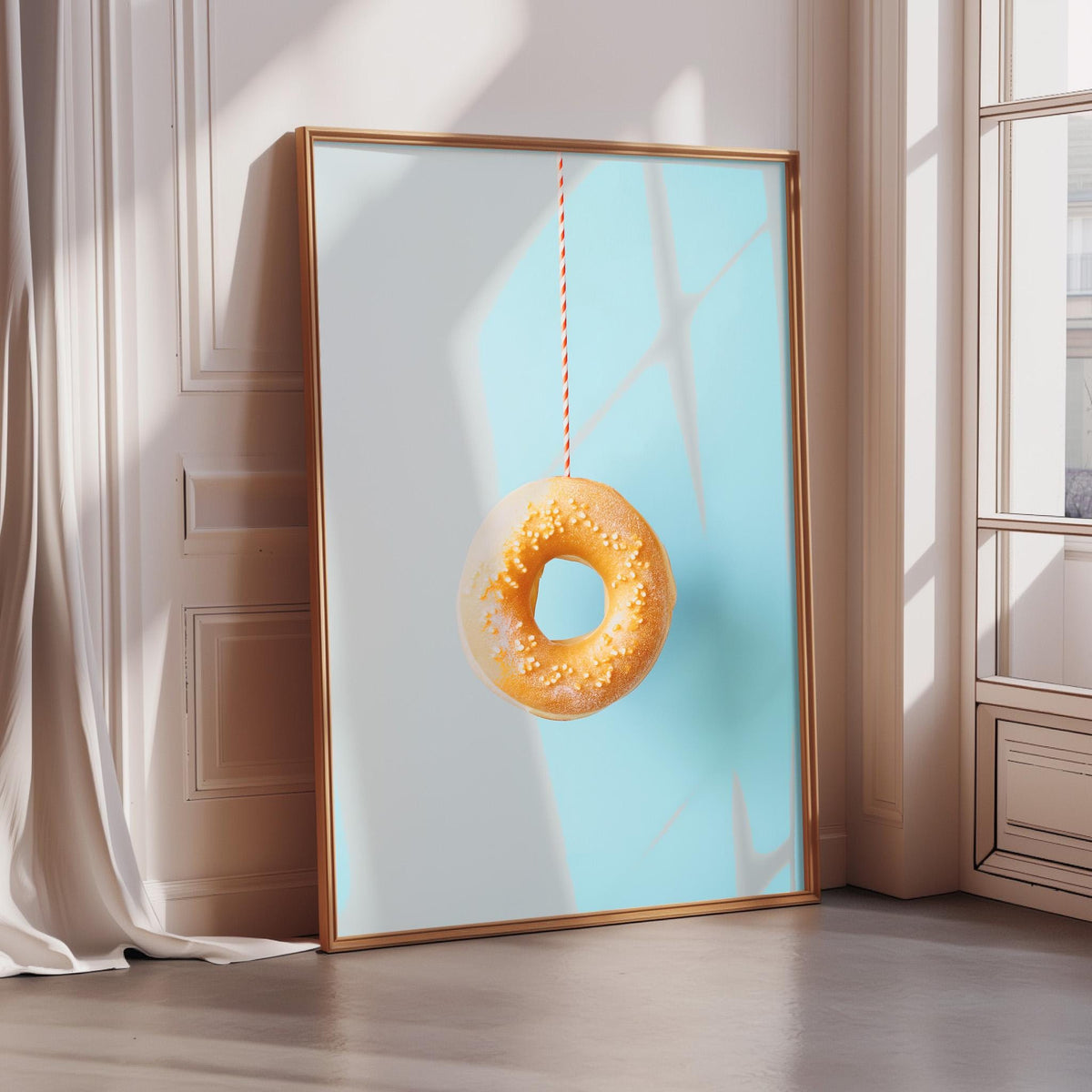 A framed image of a donut hanging from a string is displayed on a wall in a room with a window.