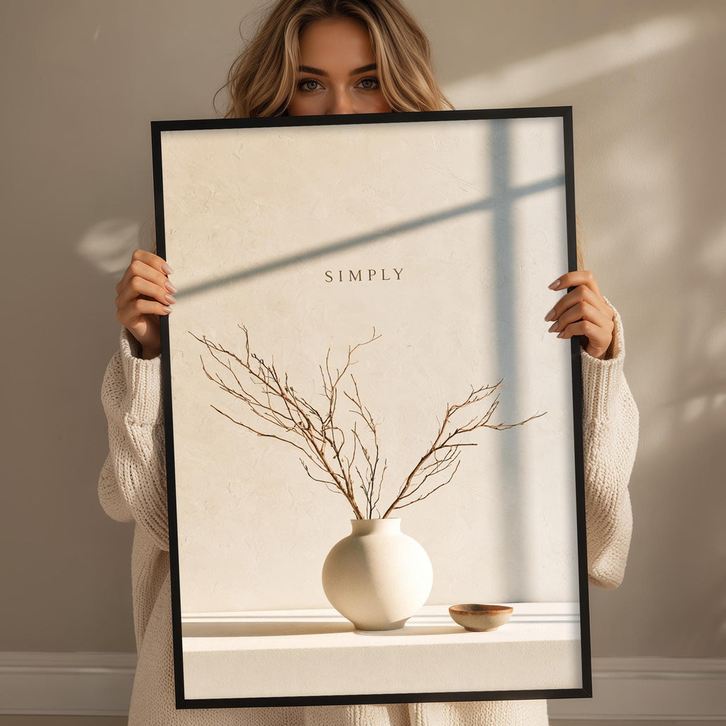A woman holding a framed print with a vase of branches and a bowl on a shelf.