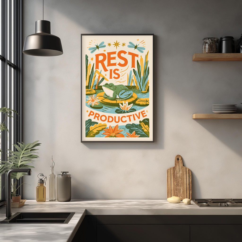 a kitchen counter with a framed poster hanging on the wall above it. The poster has a colorful design with a frog and plants, and the text "REST IS PRODUCTIVE" is written on it.