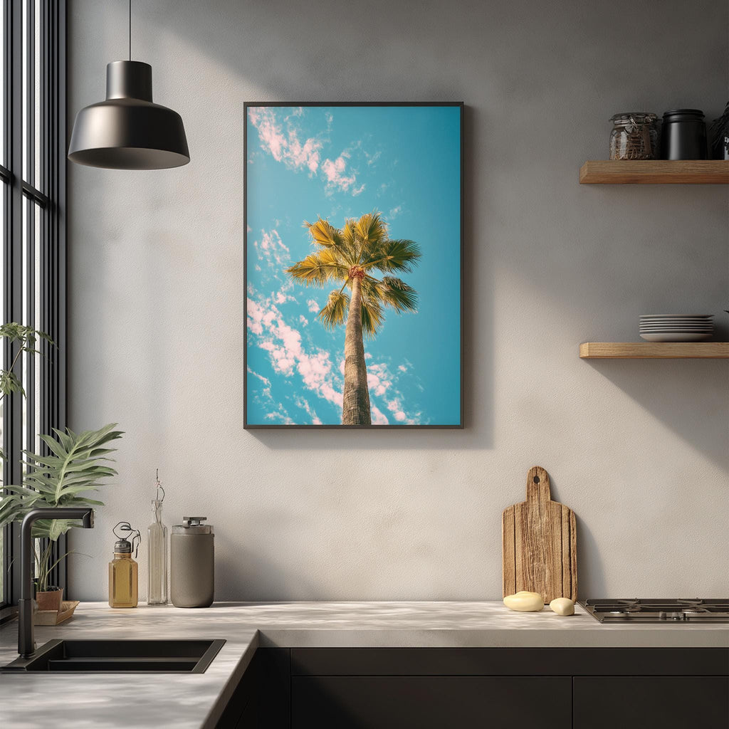 a kitchen counter with a framed picture of a palm tree on the wall above it. The kitchen counter has various items on it, including a cutting board, a bottle, and a vase.