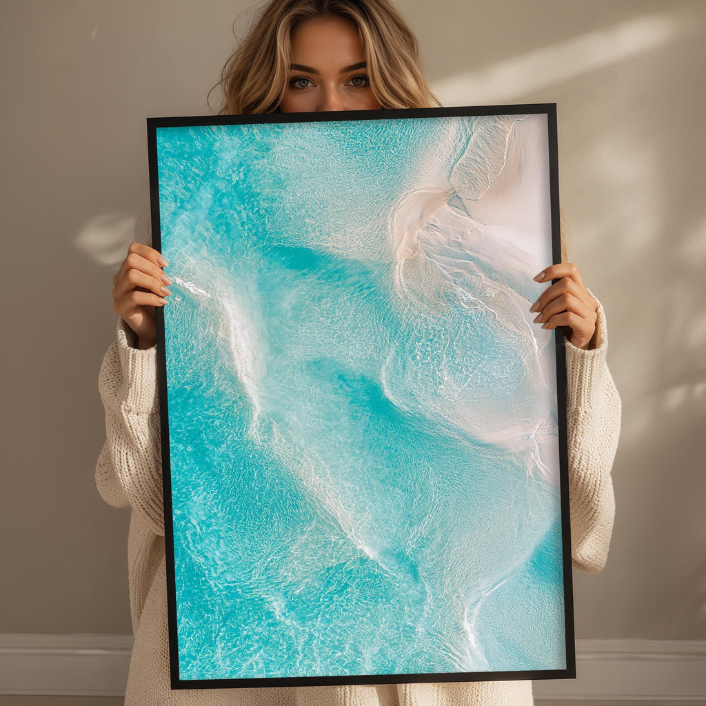 A woman holds up a framed picture of a serene ocean scene, featuring a blend of blue and white hues.