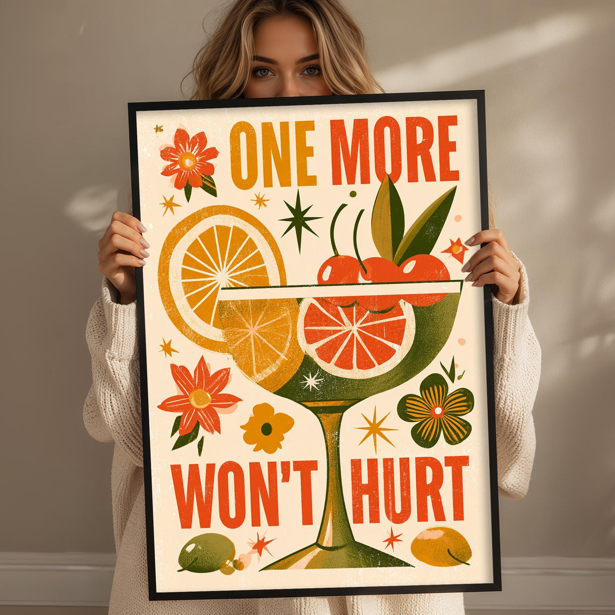 A woman is holding up a framed poster with a colorful design featuring various fruits and flowers, along with the text "One more won't hurt".
