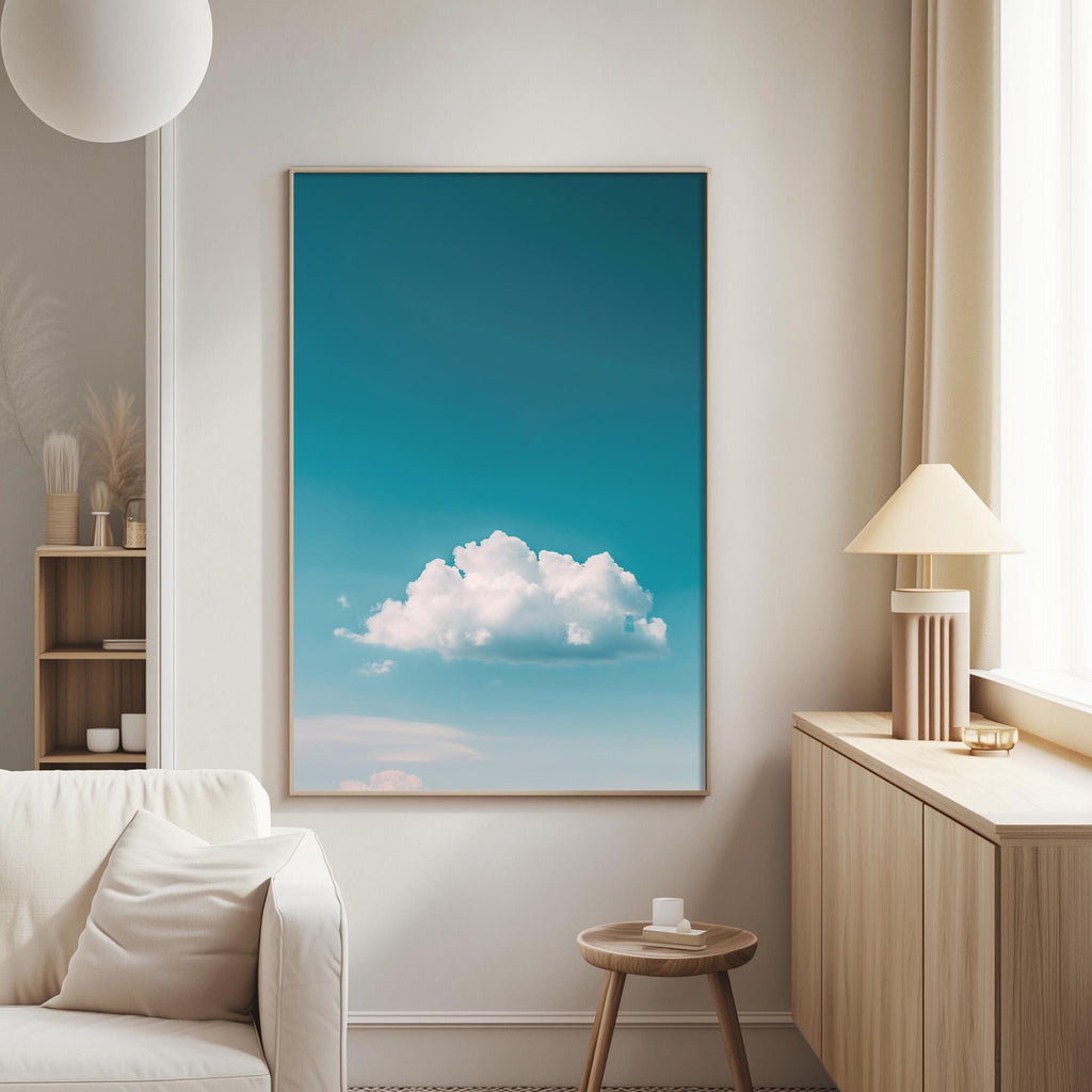 a serene living room with a large framed picture of a blue sky and fluffy white clouds hanging on the wall. The room is furnished with a white sofa, a wooden side table, and a lamp on a wooden cabinet.
