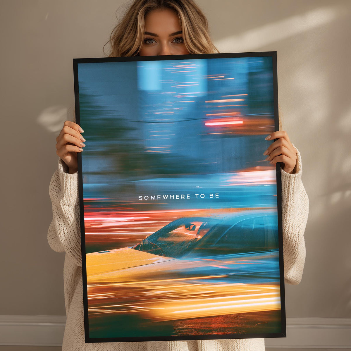 A woman holding a framed poster with a blurred car and colorful background.