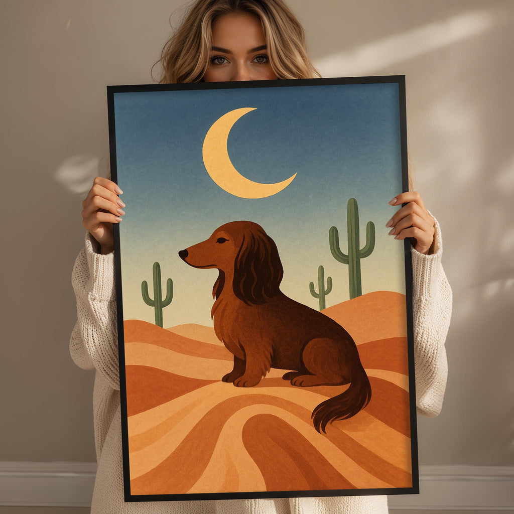 A woman holds up a framed illustration of a dachshund dog in a desert landscape, with cacti and a crescent moon in the background.