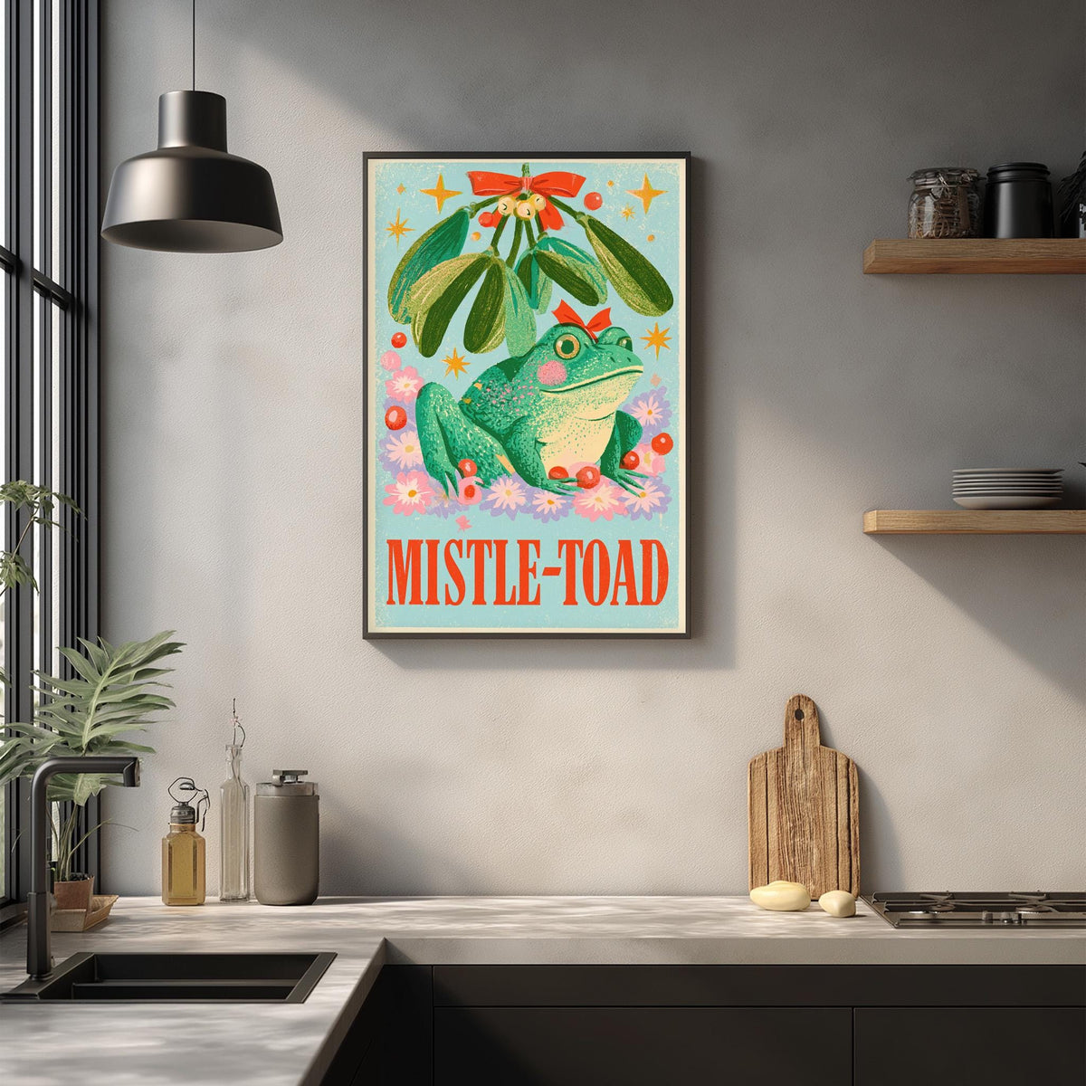 a framed poster of a green frog with a mistletoe on a wall above a kitchen counter.