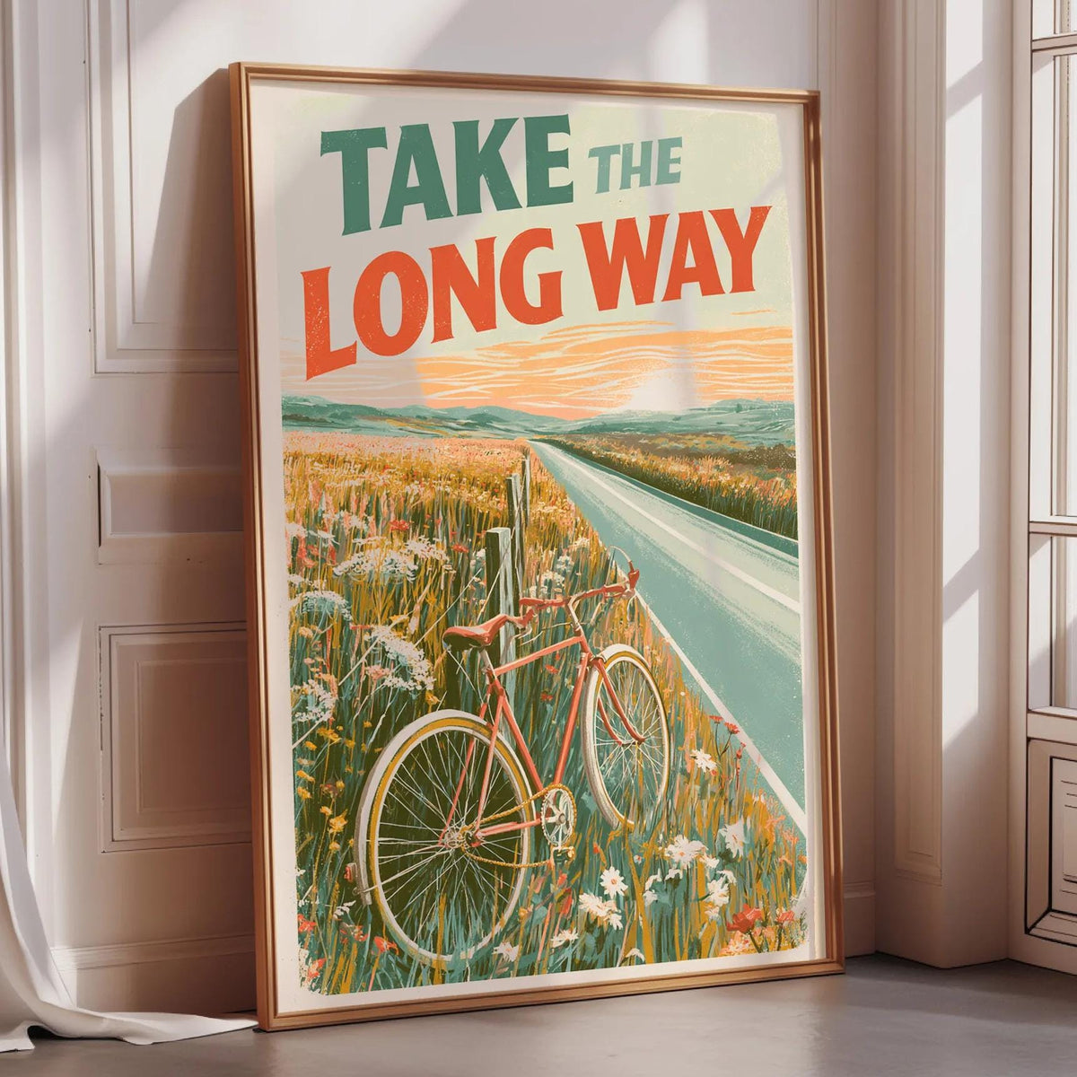 a framed poster with a bicycle and a scenic landscape, including a road and a field with flowers.