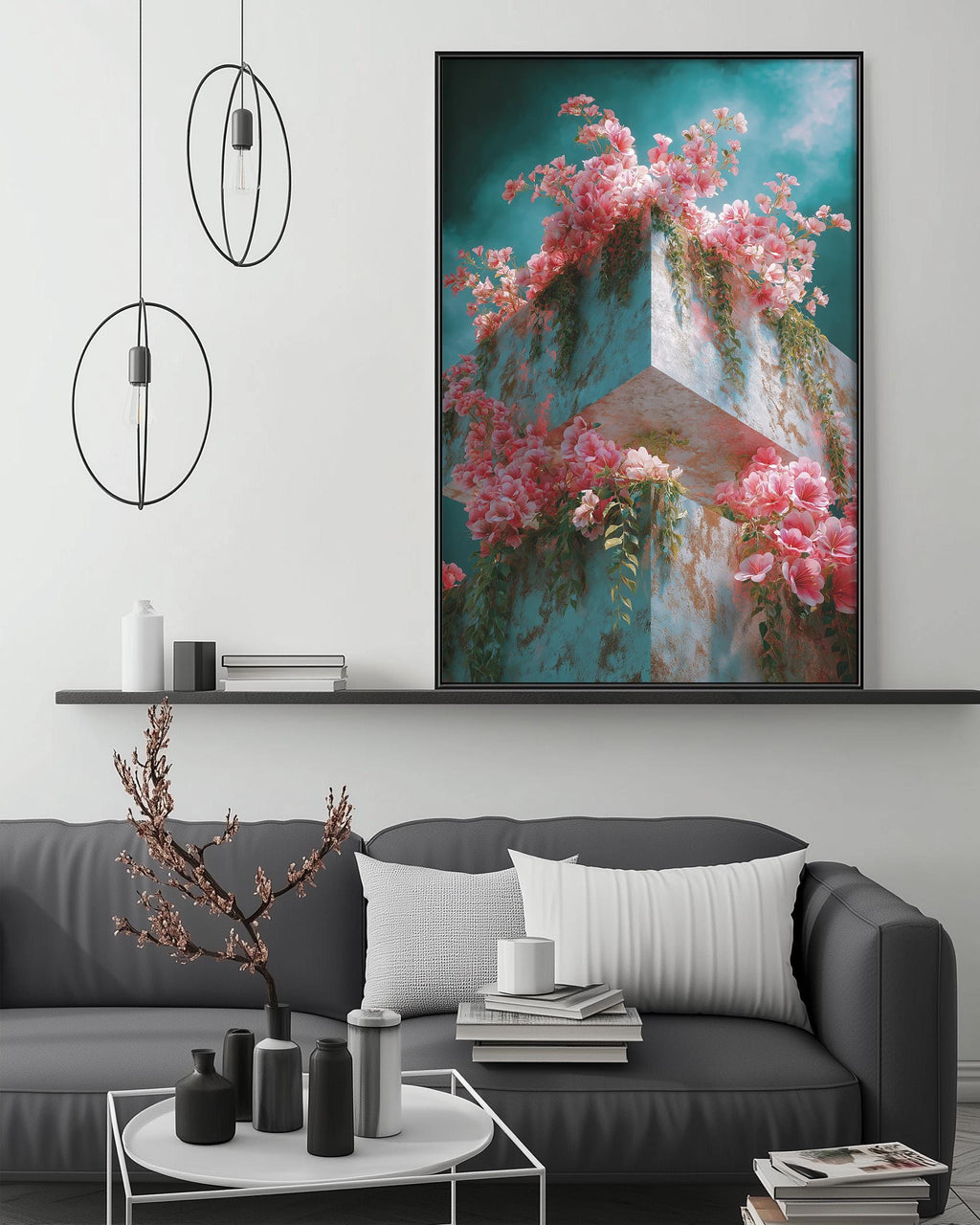 a large framed picture of pink flowers hanging on a wall above a gray couch with white pillows. The couch is positioned in front of a coffee table with various decorative items, such as vases and books. The overall setting appears to be a cozy and stylish living room.