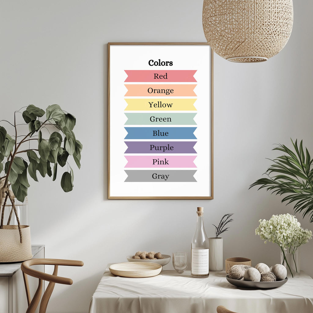 a framed poster with color names on it, hanging on a wall above a dining table with various items on it, such as a bottle, bowls, and a vase.