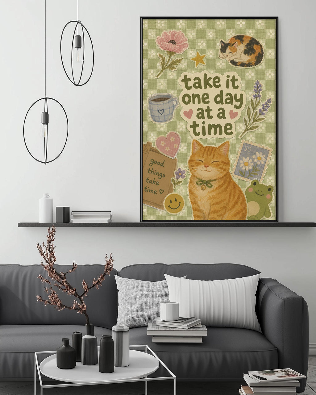 a cozy living room with a gray couch, a coffee table, and a framed poster on the wall. The poster has a cheerful design with a cat, flowers, and a quote that says "Take it one day at a time".