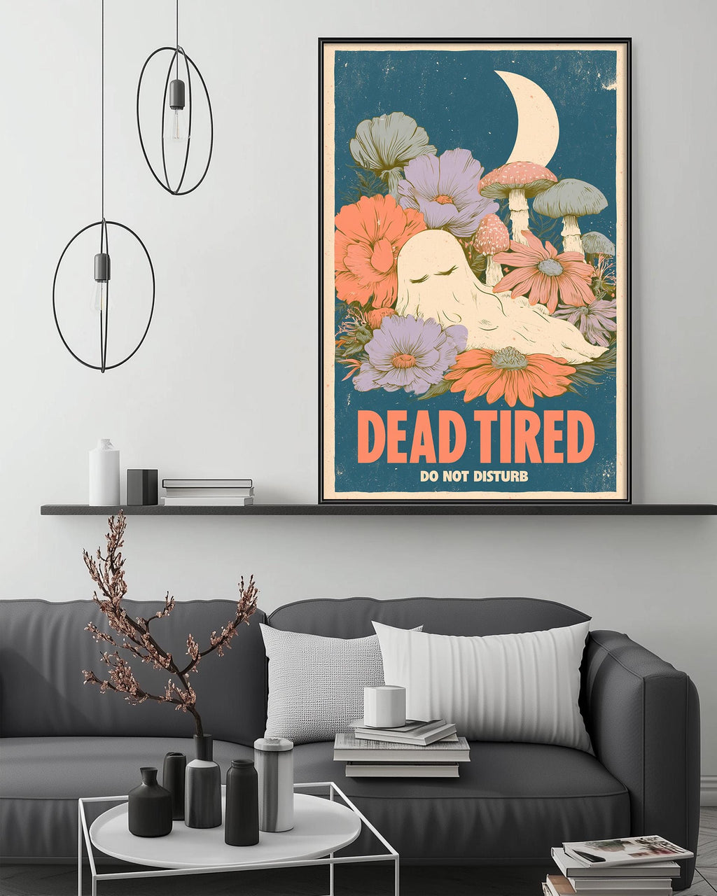 a poster with a whimsical illustration of a sleeping ghost surrounded by flowers and mushrooms, hanging on a wall above a gray couch.