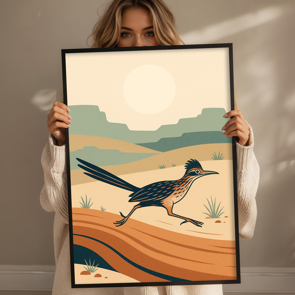 A woman is holding up a framed print of a bird in a desert landscape, with mountains in the background.