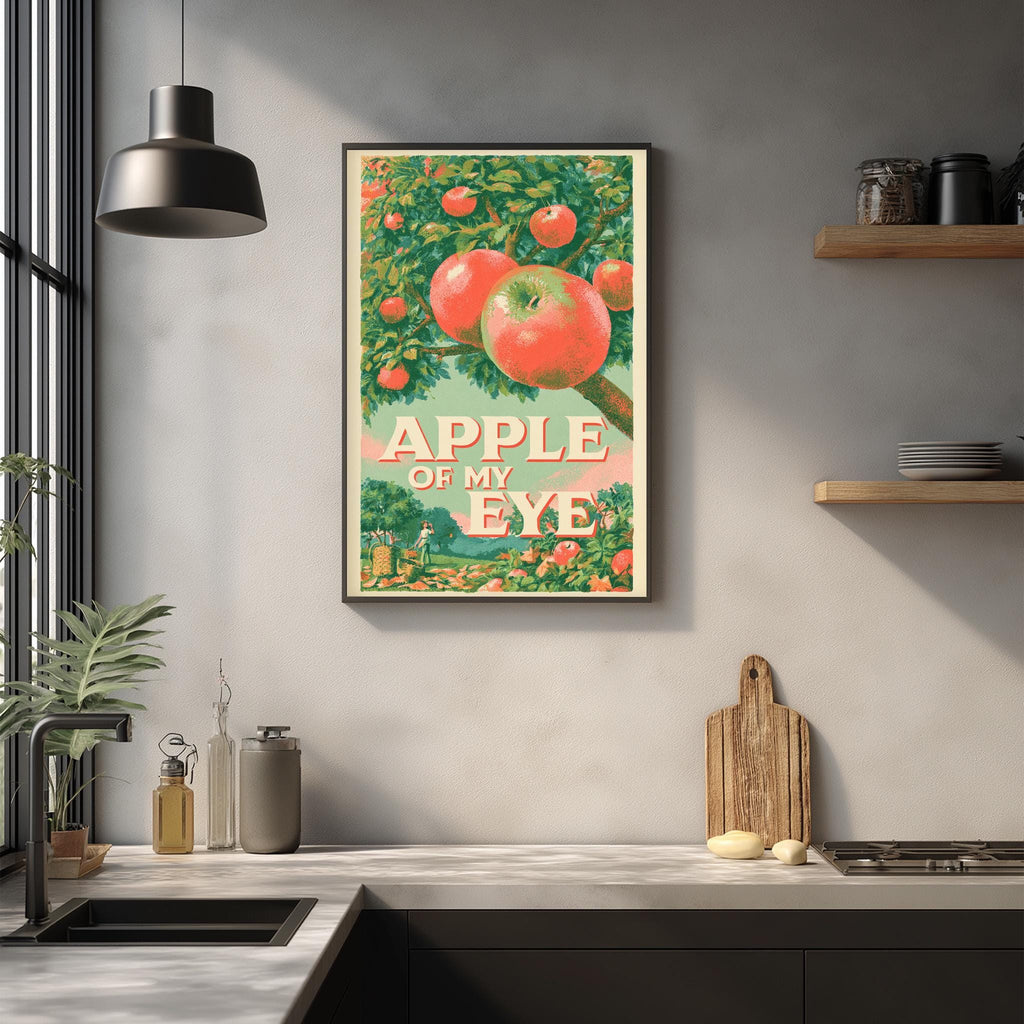 a framed vintage advertisement poster of an apple tree with the text "APPLE OF MY EYE" displayed prominently. The poster is hanging on a wall above a kitchen counter with various kitchen items such as a cutting board, a bottle, and a bowl.