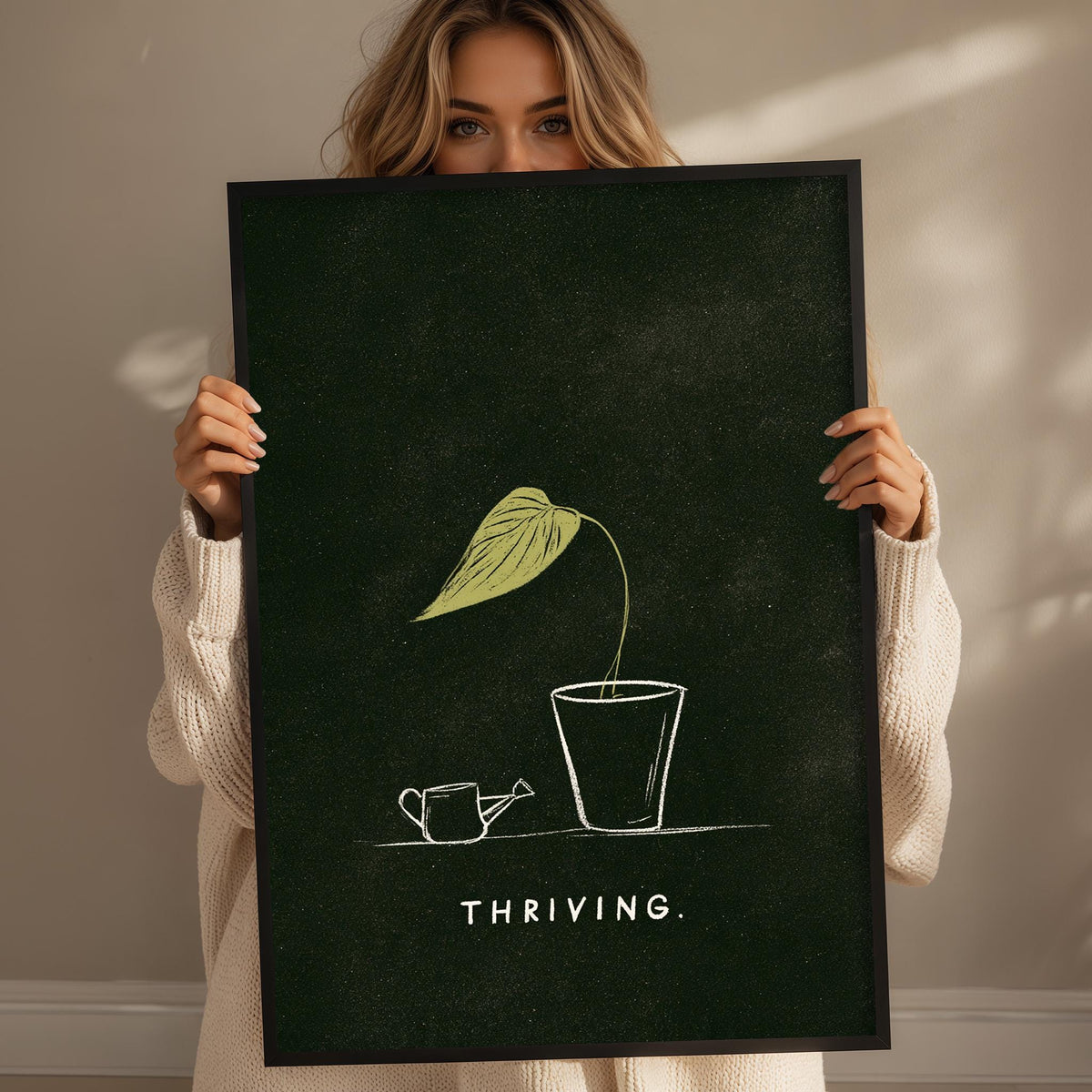 A woman holding a framed poster with a drawing of a plant and the word "THRIVING" written on it.