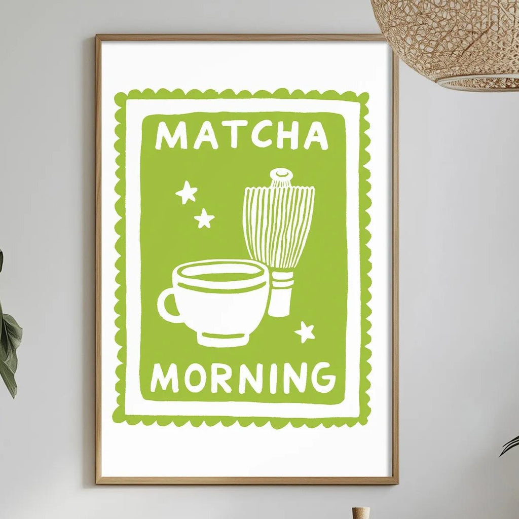 a framed poster with the text "MATCHA MORNING" hanging on a wall above a dining table with various items on it, including a bowl, a bottle, and a vase.