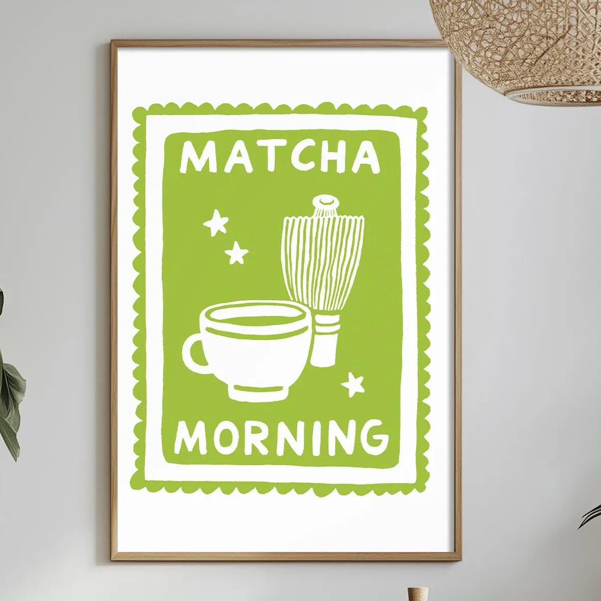 a framed poster with the text "MATCHA MORNING" hanging on a wall above a dining table with various items on it, including a bowl, a bottle, and a vase.