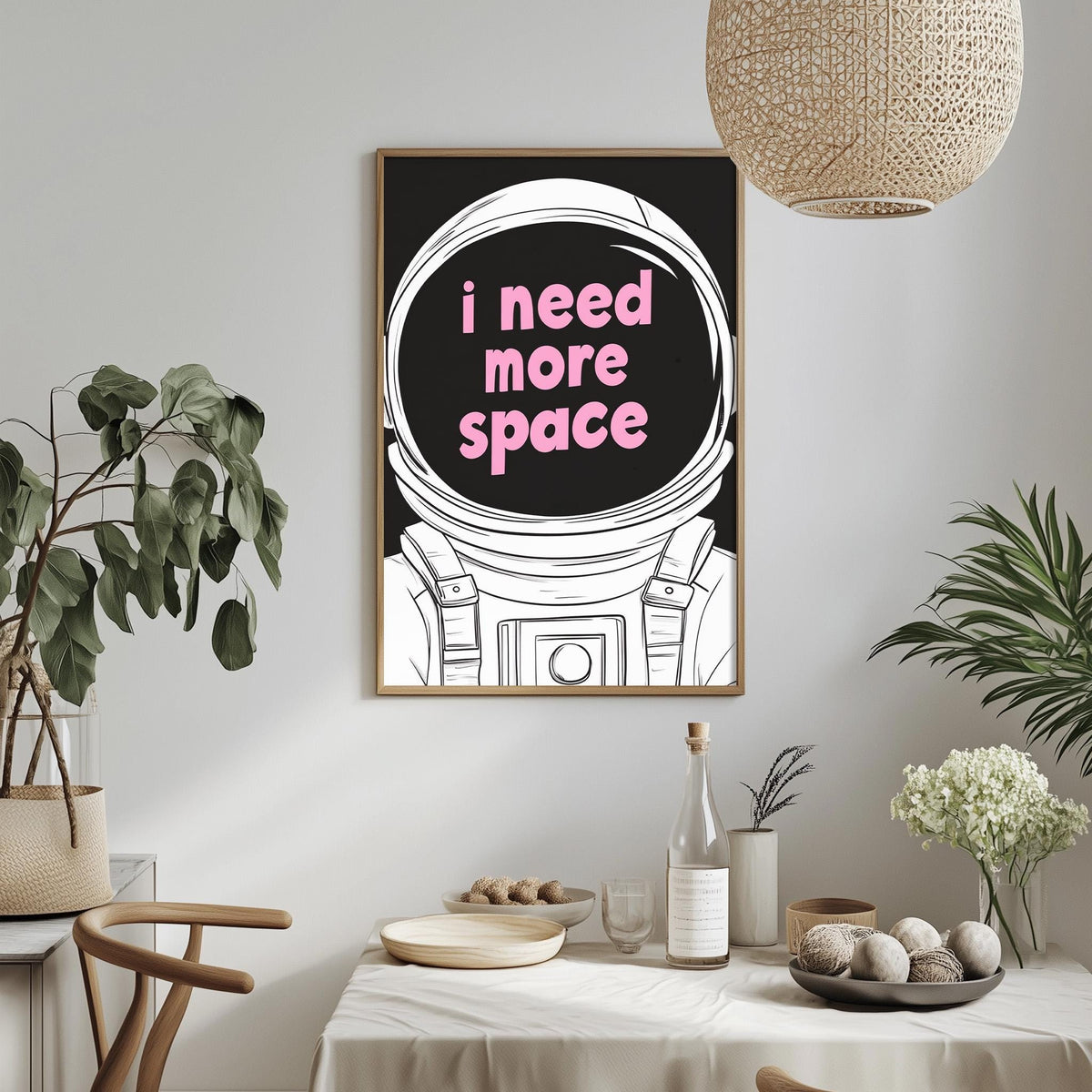 a framed poster with the text "I need more space" in pink letters, hanging on a wall above a dining table with various items on it.