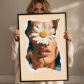 A woman holding a framed picture of a woman's face partially obscured by a large white flower.