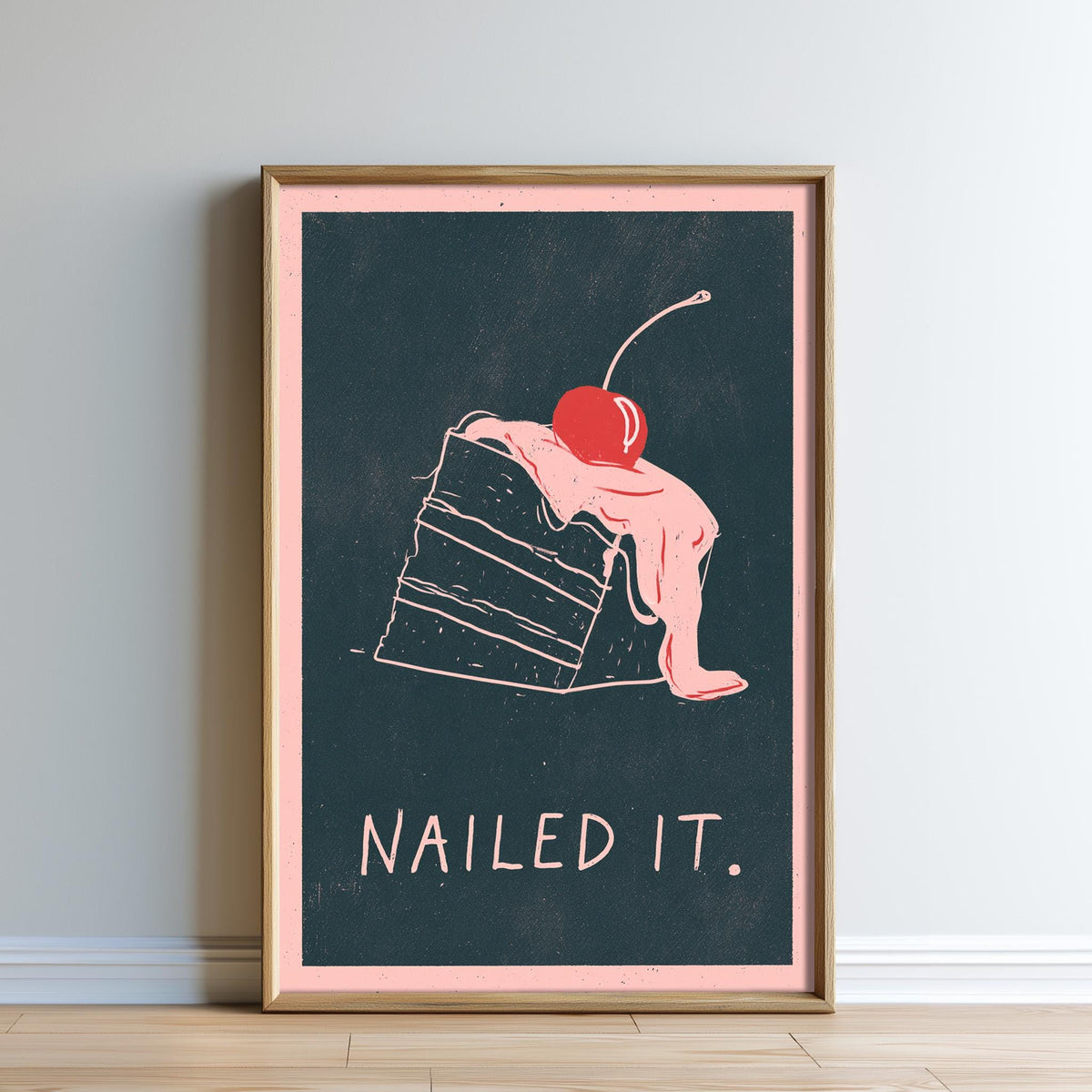 The image is a framed poster with a black background and a pink border. The poster features a drawing of a slice of cake with a cherry on top, accompanied by the text "Nailed it."