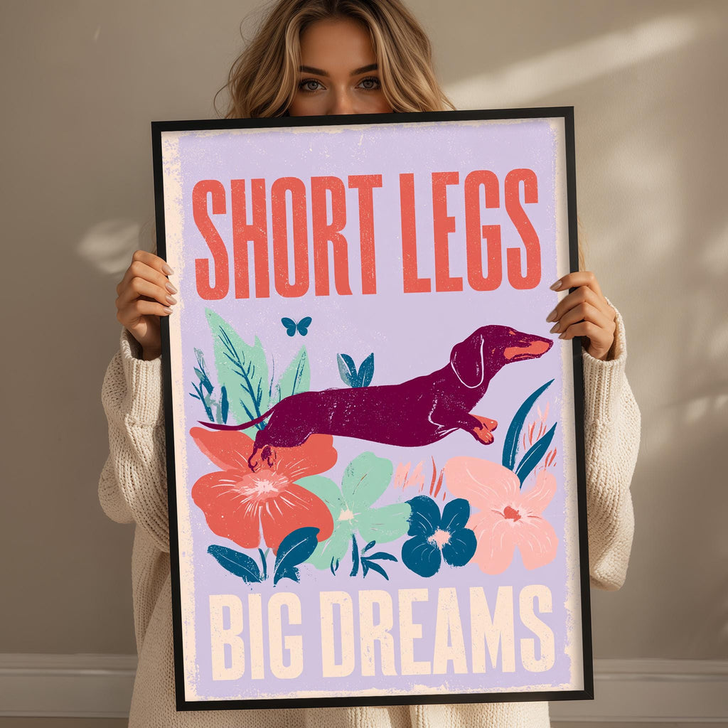 A woman holding a framed poster with a dachshund dog and colorful flowers.