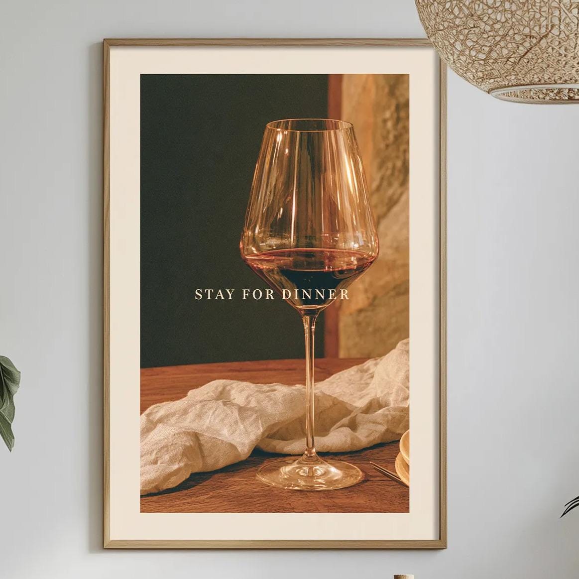 a dining table set with a wine glass, a bottle, and a bowl, along with some plants and a hanging light fixture.