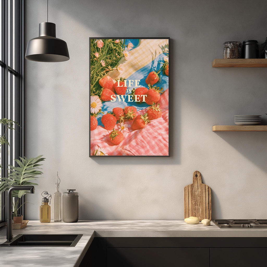 a kitchen counter with a framed poster of strawberries hanging on the wall above it. The poster has the text "LIFE SWEET" written on it.