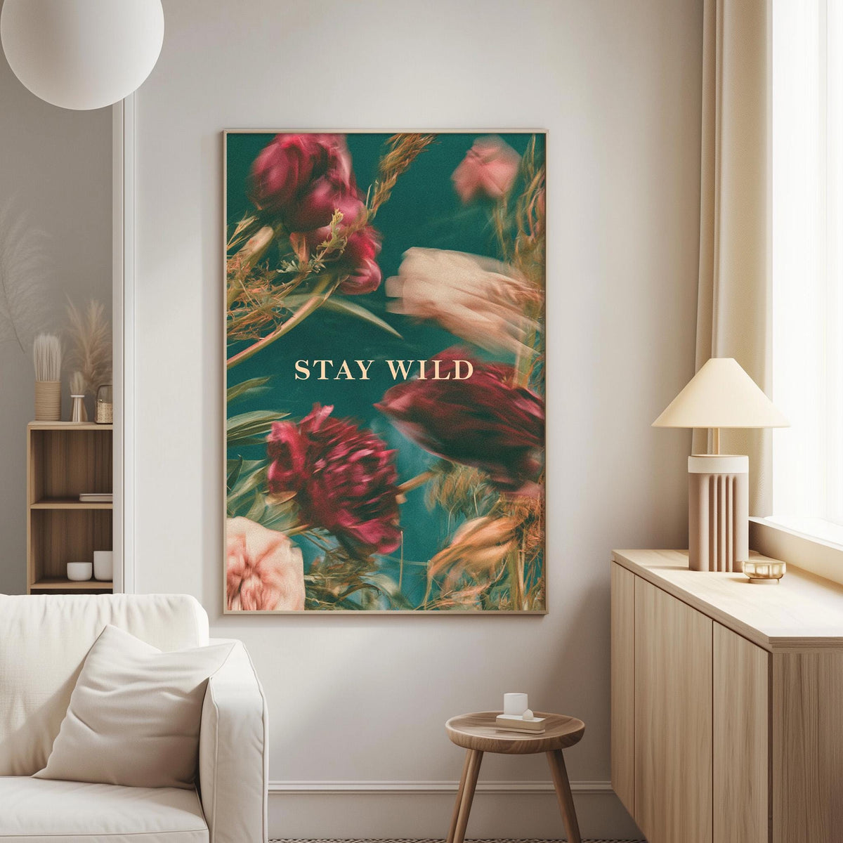 a living room with a large framed poster of a floral design on the wall, which has the text "STAY WILD" written on it. The room also includes a white couch, a small table, and a lamp.