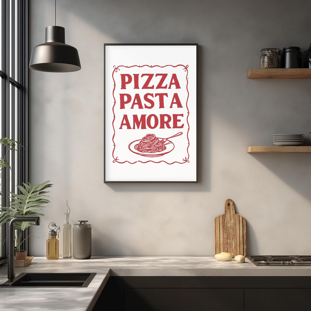 a kitchen counter with a framed poster that reads "PIZZA PASTA AMORE" above a plate of spaghetti. The poster is hanging on a wall above a sink and a wooden cutting board.