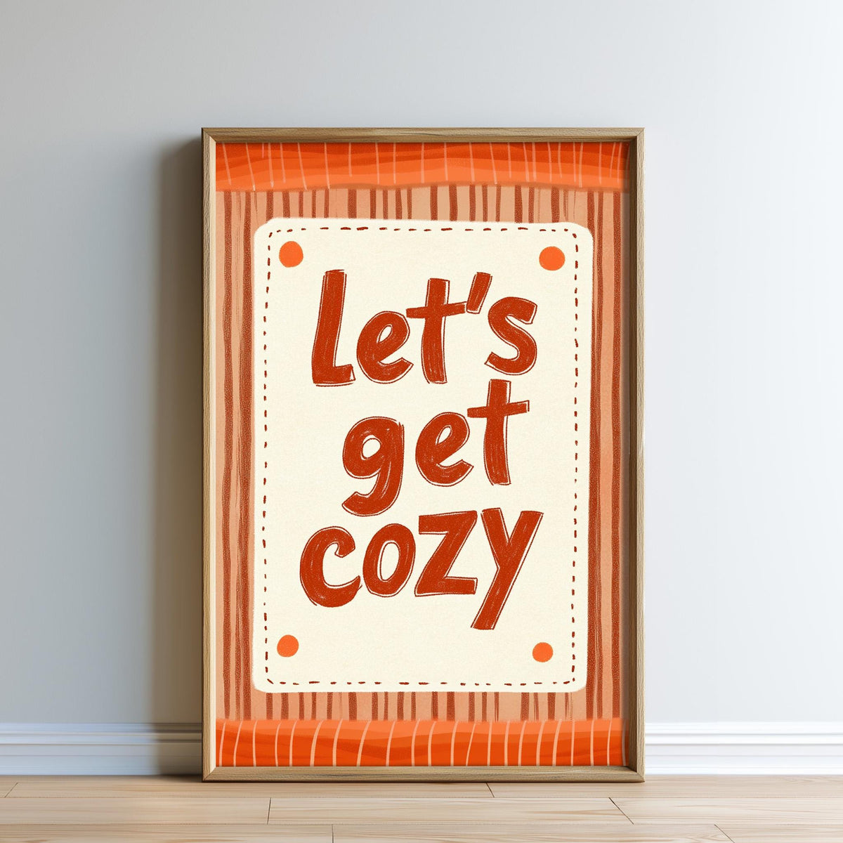 A framed poster with the text "Let's get cozy" in a playful, handwritten style.