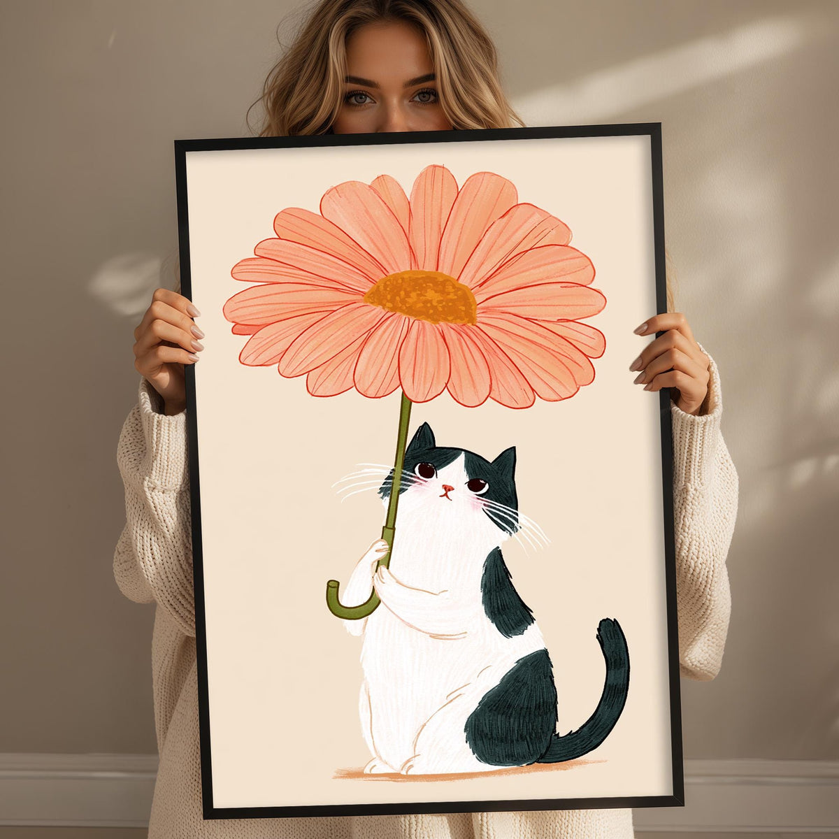 A woman holds a framed illustration of a cat sitting under a large pink flower.