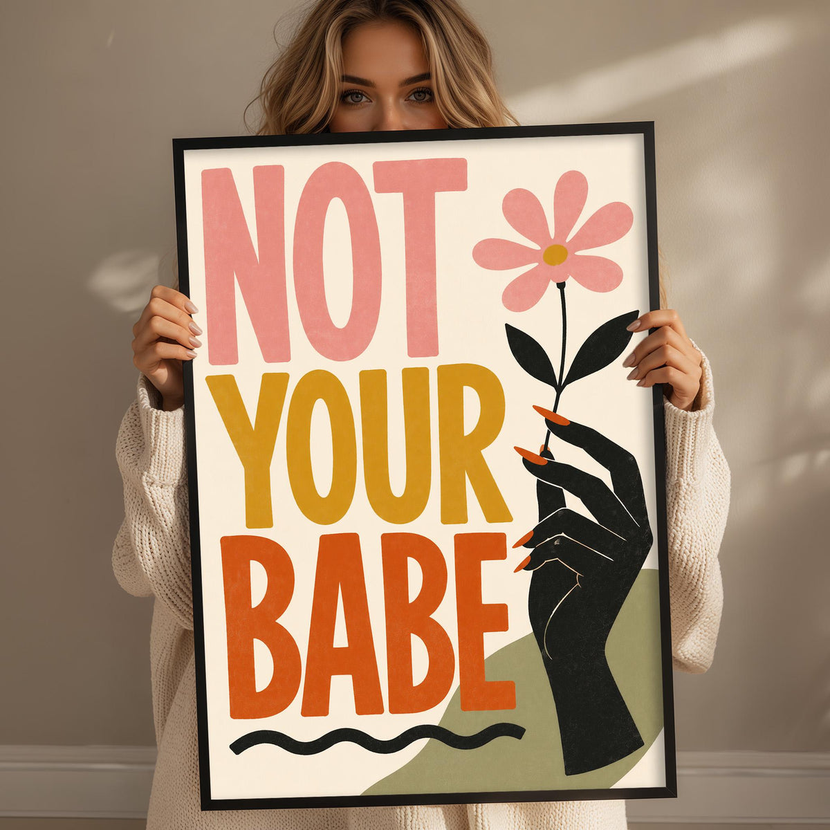 A woman holding a framed poster with the text "NOT YOUR BABE" and a flower graphic.