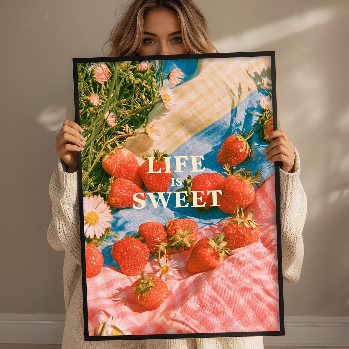 A woman holds up a framed poster with a vibrant image of strawberries and flowers, with the text "LIFE IS SWEET" prominently displayed.