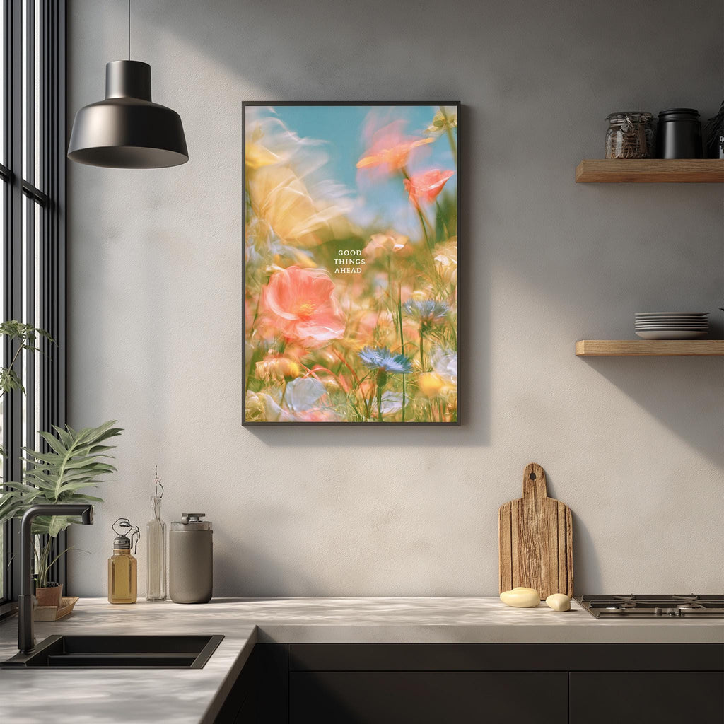 a kitchen counter with a framed poster of a colorful garden scene hanging above it. The poster has a blue sky and flowers in the background, creating a vibrant and cheerful atmosphere. The kitchen counter also has various items such as a cutting board, a bottle, and a bowl, suggesting a functional and organized space.