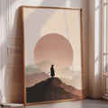 a large framed poster depicting a silhouetted figure of a person standing on a mountain peak against a backdrop of a sunset.