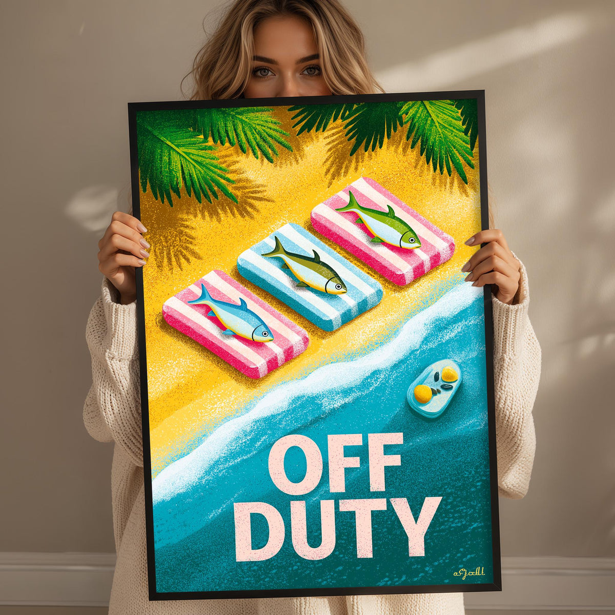 A woman is holding up a framed poster with a beach scene and three fish on it.