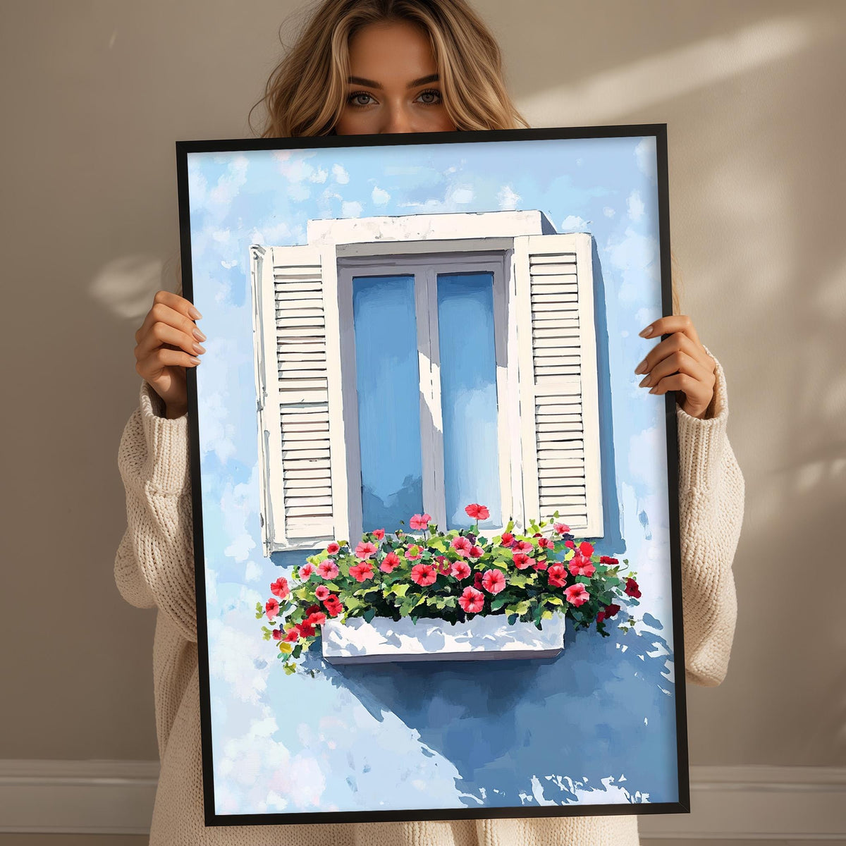A woman holds up a framed painting of a window with a flower box filled with red and pink flowers.