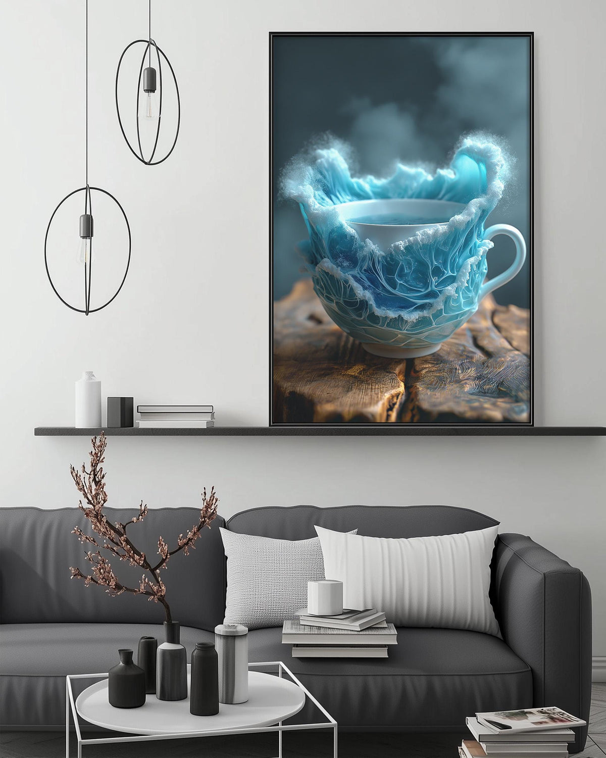 a large framed artwork depicting a teacup with a blue and white design, placed on a wooden surface. The artwork is hanging on a wall above a gray couch, which has a coffee table in front of it. The room has a minimalist and modern design, with a black pendant light hanging above the artwork and a white shelf below it.