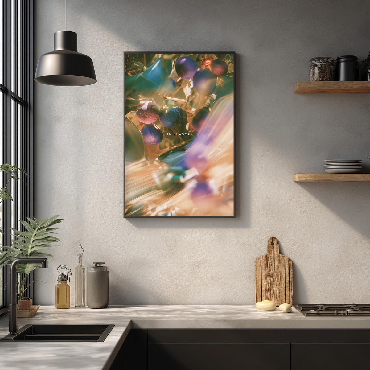 a kitchen counter with various items such as a cutting board, a plant, and a bottle. Above the counter, there is a framed picture hanging on the wall, depicting a blurry image of grapes.