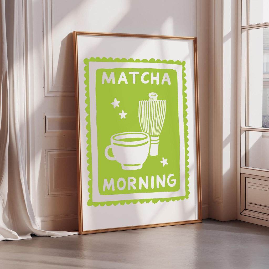A framed poster with a green border and white text, depicting a cup and a whisk, along with the text "MATCHA MORNING".