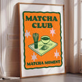 The image is a framed poster with an illustration of matcha-making equipment and a bowl of matcha on a tray, along with the text "MATCHA CLUB MATCHA MOMENT" and three stars.