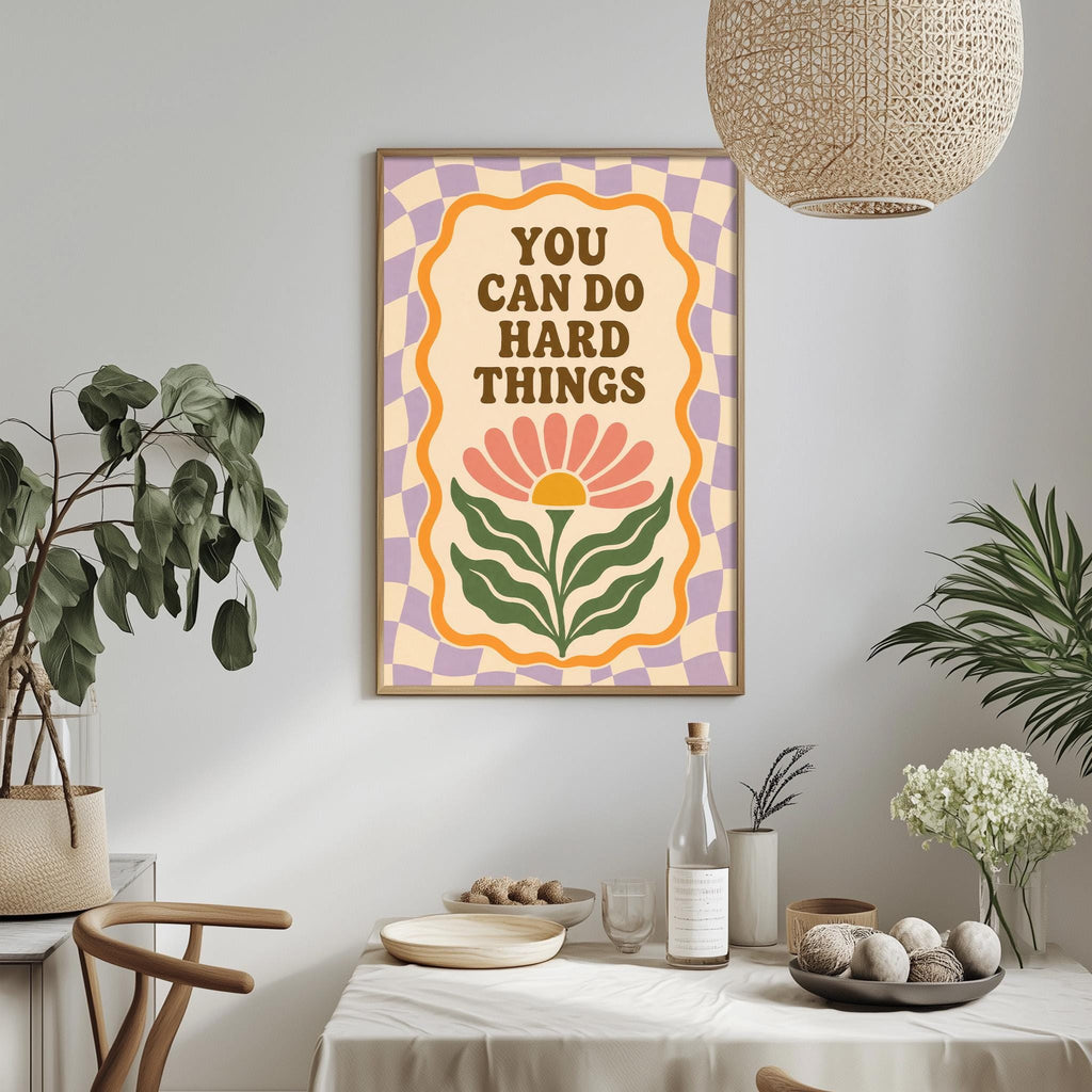 a framed poster with the text "YOU CAN DO HARD THINGS" hanging on a wall above a dining table with various items on it.