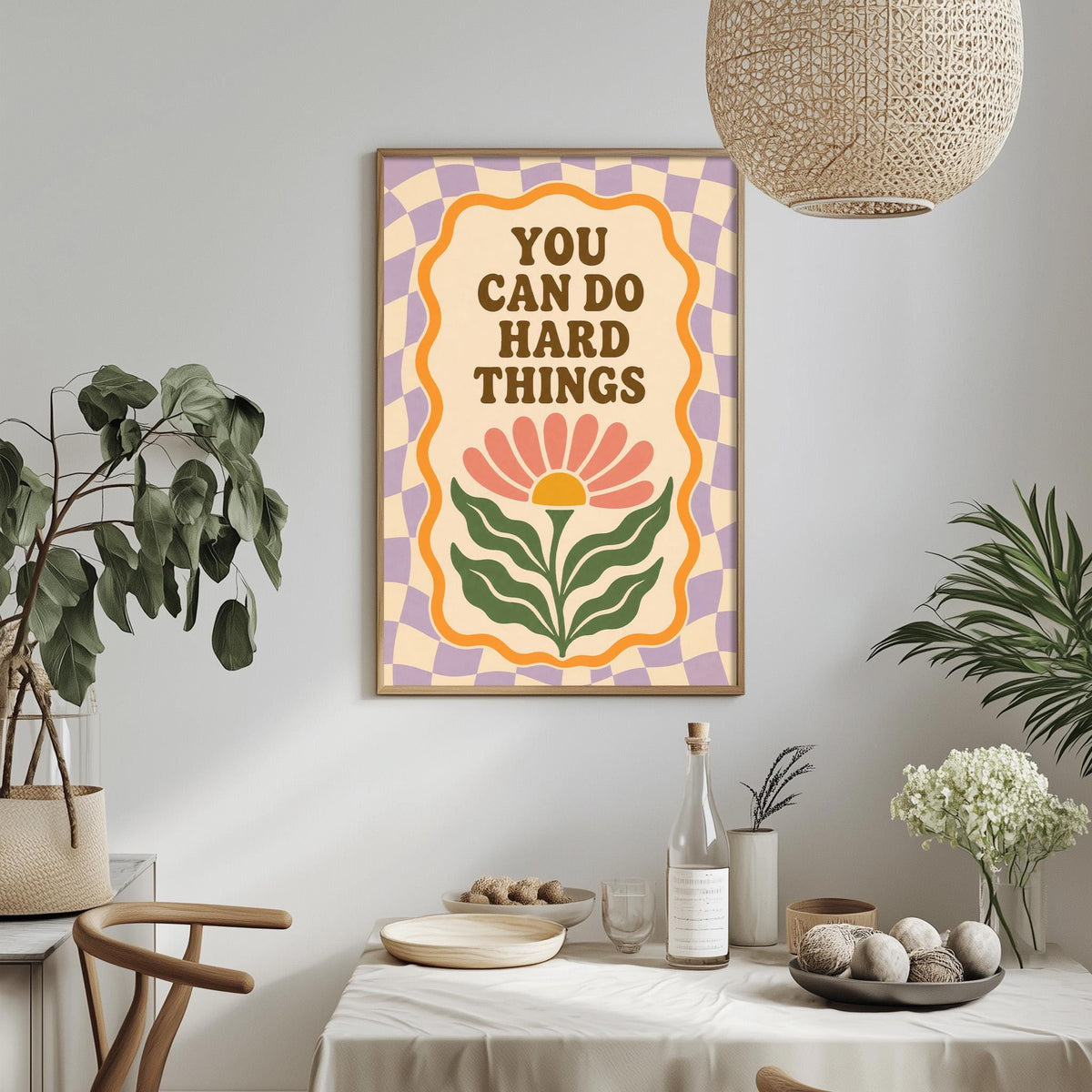 a framed poster with the text "YOU CAN DO HARD THINGS" hanging on a wall above a dining table with various items on it.